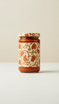 A perfectly centered, straight-on shot of a gourmet roasted red pepper dip jar on a simple, Almond Milk colored...